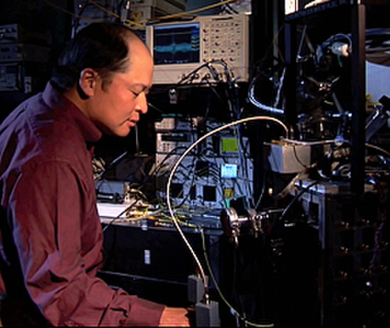 Pesquisador do NIST operando bancada de detecção de fótons com osciloscópios e fibras ópticas.